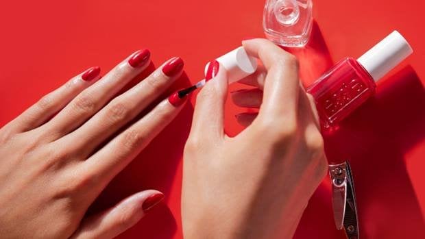 Mains d’une personne avec une manucure rouge appliquant une couche de finition sur ses ongles