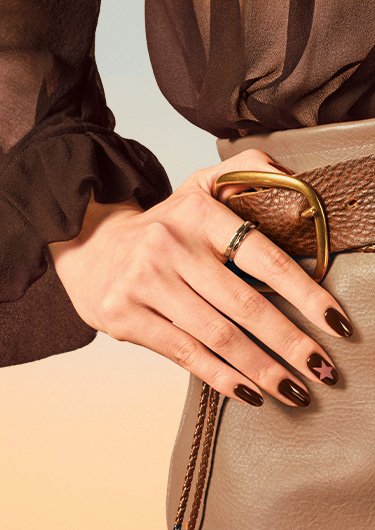 Three bottles of boho rodeo polish on a rock next to light skin hand on hip wearing brown polish
