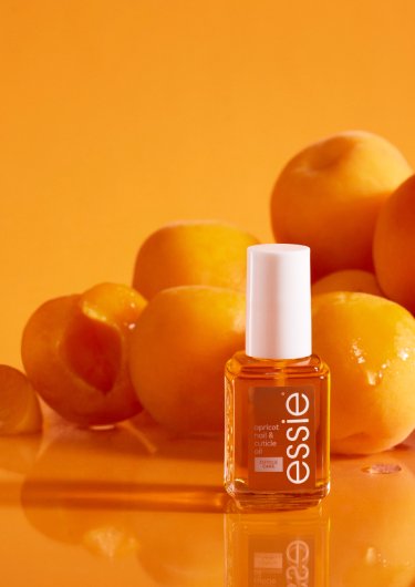 Huile pour cuticules essie dans une bouteille classique et en format avec applicateur à bille, avec des abricots en arrière-plan