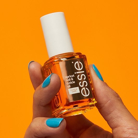 Main avec manucure bleue tenant l’huile pour ongles et cuticules à l’abricot d’essie en format classique