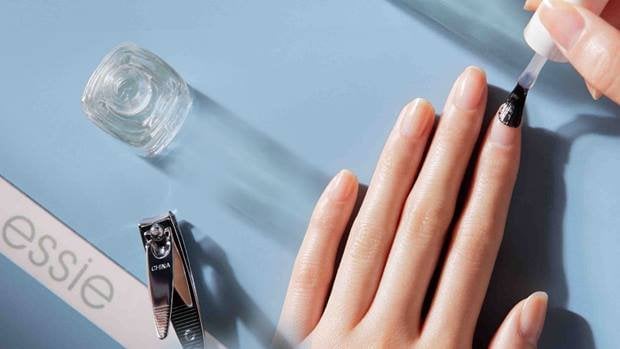 Mains d’une personne appliquant un traitement fortifiant sur ses ongles, entourées d’outils pour les ongles